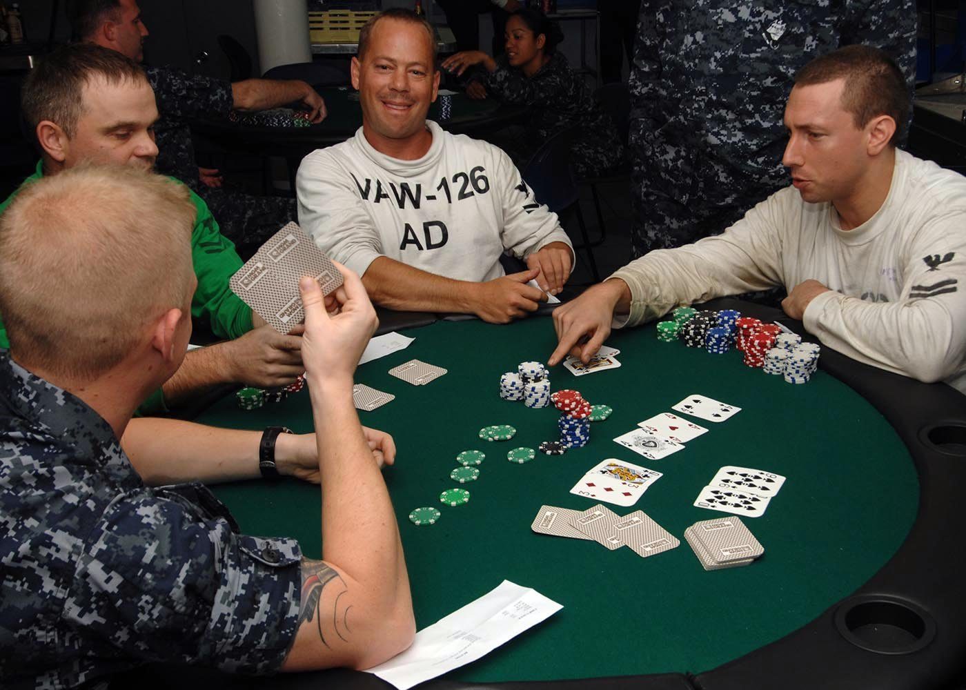 Cuatro marineros juegan Texas Hold'em en una mesa de fieltro verde con fichas apiladas y cartas comunitarias boca arriba