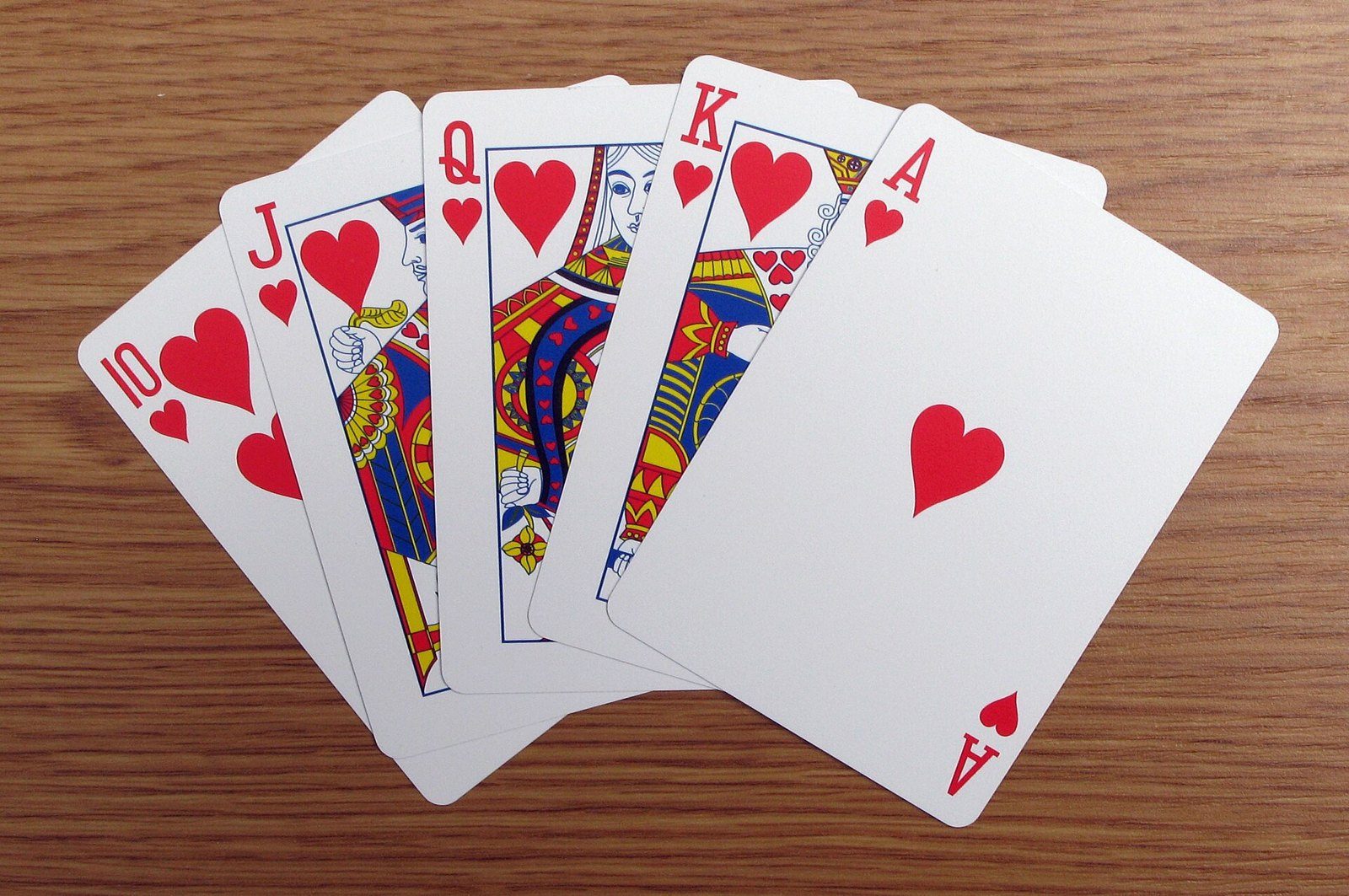 Escalera real de corazones, del 10 al as, con las cartas abiertas en abanico sobre una mesa de madera