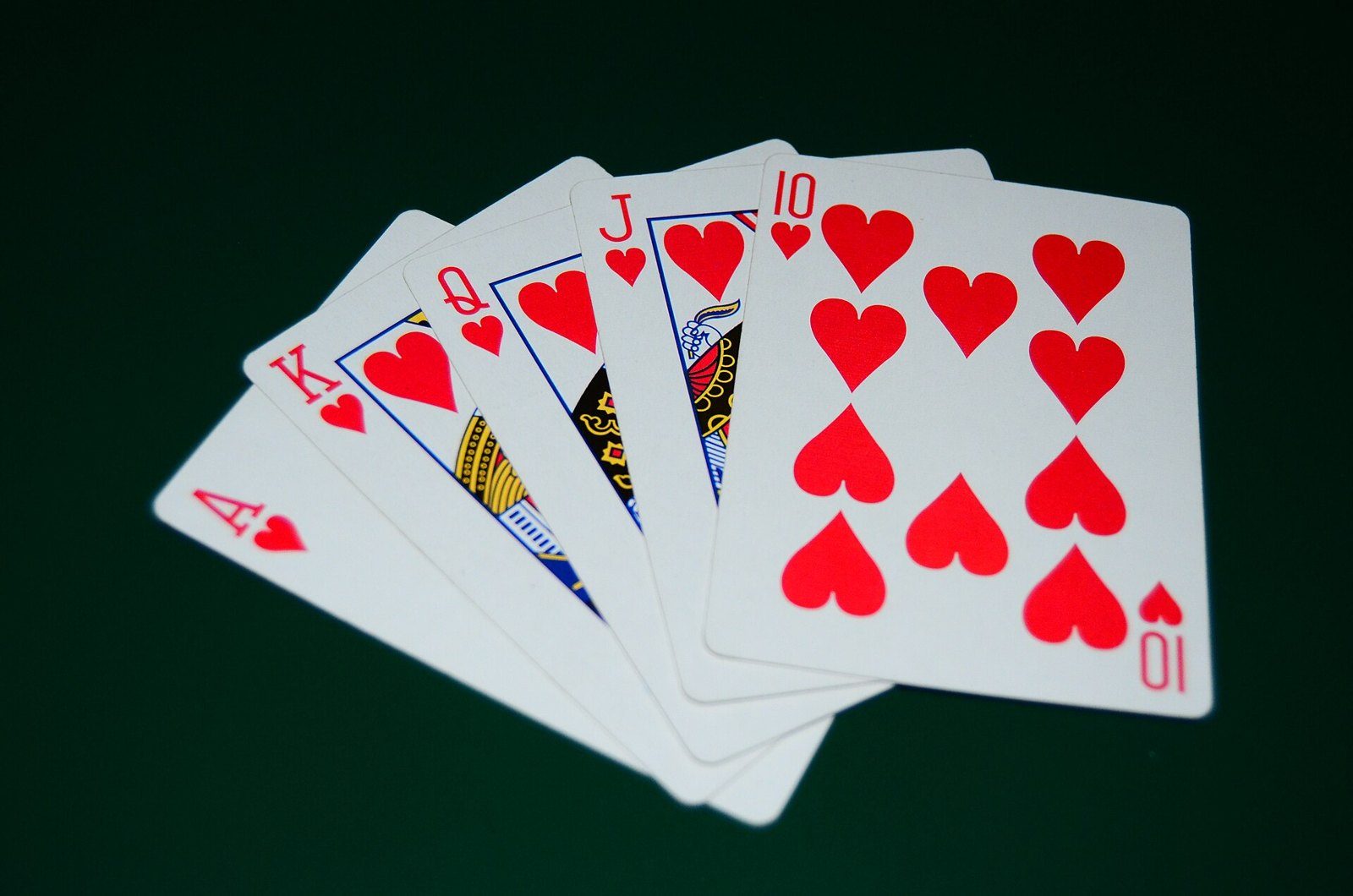Cinco cartas abiertas en abanico, del 10 al as de corazones, sobre fondo oscuro: una escalera real de corazones