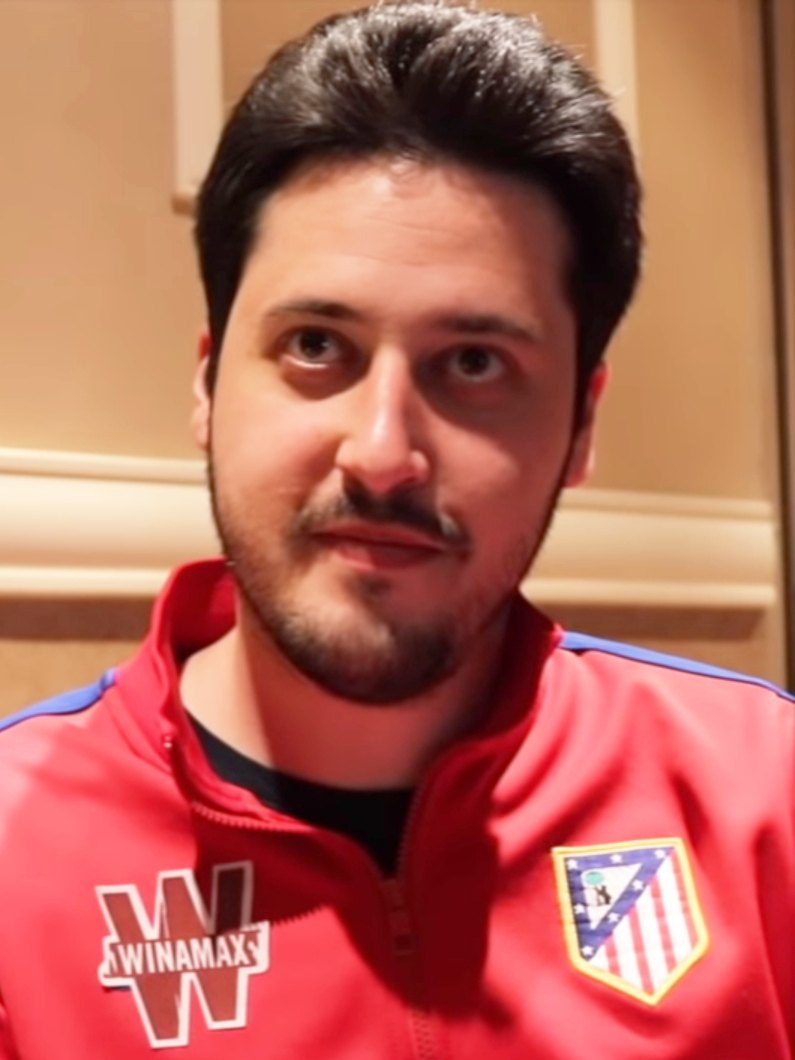 Retrato de Adrián Mateos, hombre de pelo oscuro y barba corta, con una chaqueta deportiva roja con el escudo del Atlético de Madrid, durante una entrevista